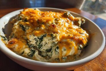 Close-up of a serving of Cheesy Chicken and Spinach Bake Comfort Meal topped with melted, slightly browned cheddar cheese.