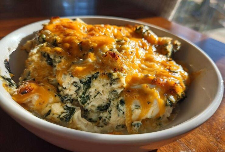 Close-up of a serving of Cheesy Chicken and Spinach Bake Comfort Meal topped with melted, slightly browned cheddar cheese.
