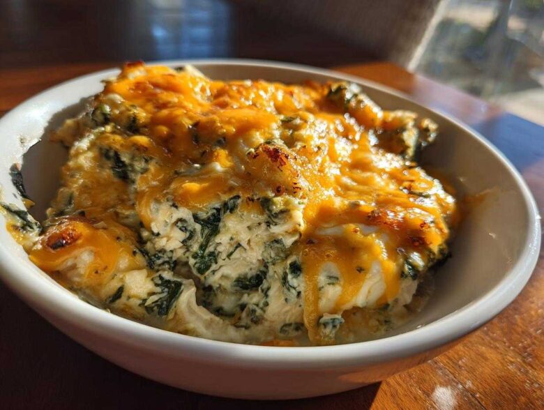 Close-up of a serving of Cheesy Chicken and Spinach Bake Comfort Meal topped with melted, slightly browned cheddar cheese.