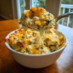 A spoonful of Cheesy Chicken and Spinach Bake Comfort Meal showing a dramatic cheese pull over a white bowl.