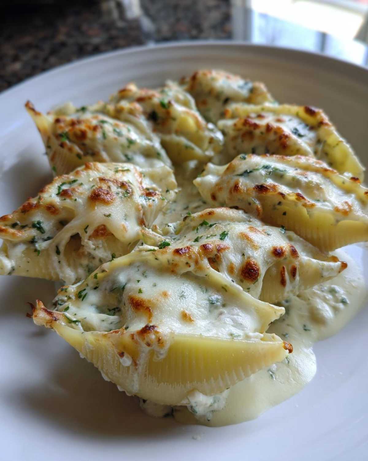 Close-up of baked Cheesy Chicken Stuffed Pasta shells covered in melted, browned cheese and white cream sauce.