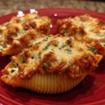 Three baked Cheesy Chicken Stuffed Shells with Spinach, topped with melted, browned cheese and parsley on a red plate.
