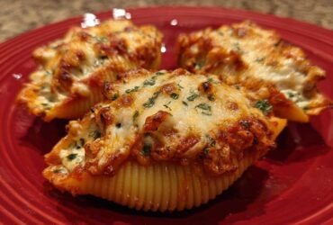 Three baked Cheesy Chicken Stuffed Shells with Spinach, topped with melted, browned cheese and parsley on a red plate.