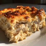 Close-up of a serving of Cheesy Chicken Tortilla Bake showing shredded chicken in a creamy sauce and a golden, bubbly cheese crust.