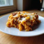 A close-up serving of Cheesy Ground Beef Pasta Bake with creamy sauce and melted mozzarella topping on a white plate.