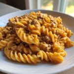 A close-up shot of spiral pasta coated in a rich, creamy, orange-hued sauce mixed with ground beef, served on a white plate.