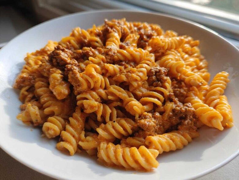 A close-up of Cheesy Ground Beef Pasta with Creamy Sauce featuring rotini pasta coated in an orange sauce with visible ground beef.