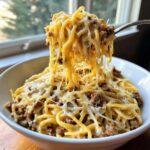 A fork lifting a generous portion of Cheesy Ground Beef Pasta with Garlic Cream Sauce, showing long cheese pulls.