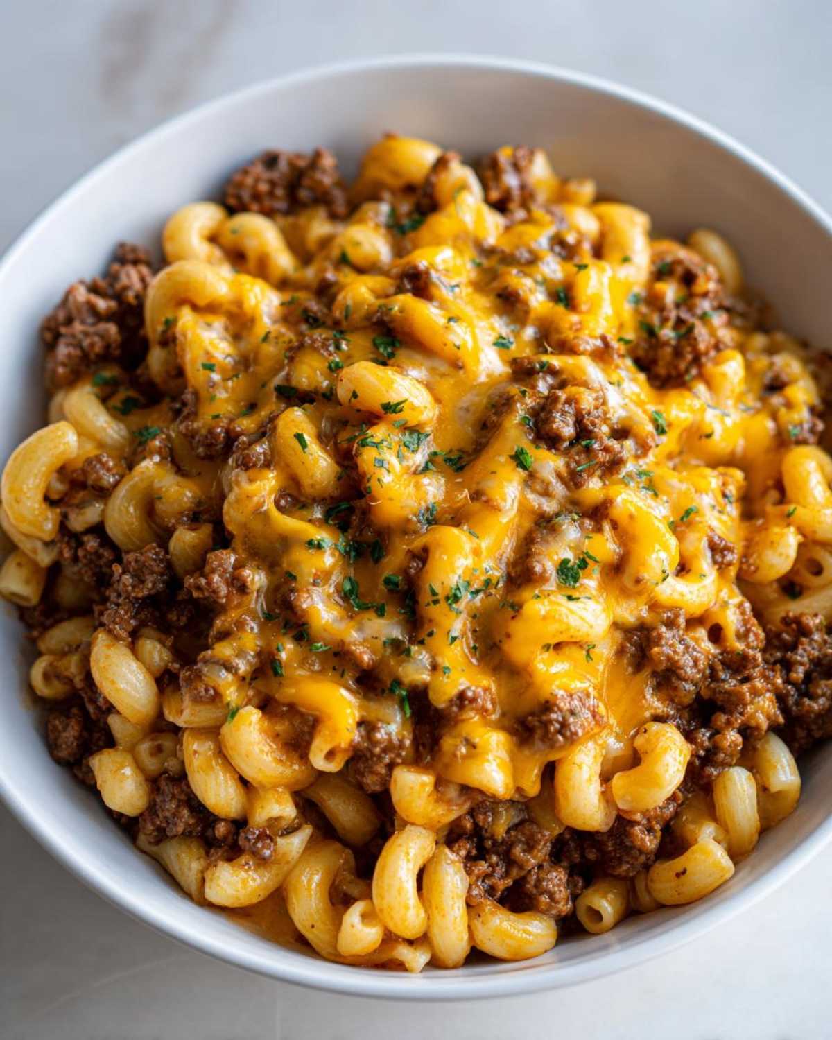 Close-up of Cheesy Ground Beef Pasta Skillet in a white bowl, topped with melted cheddar and parsley.