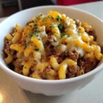 Close-up of Cheesy Ground Beef Pasta Skillet with melted cheddar and mozzarella, topped with parsley in a white bowl.
