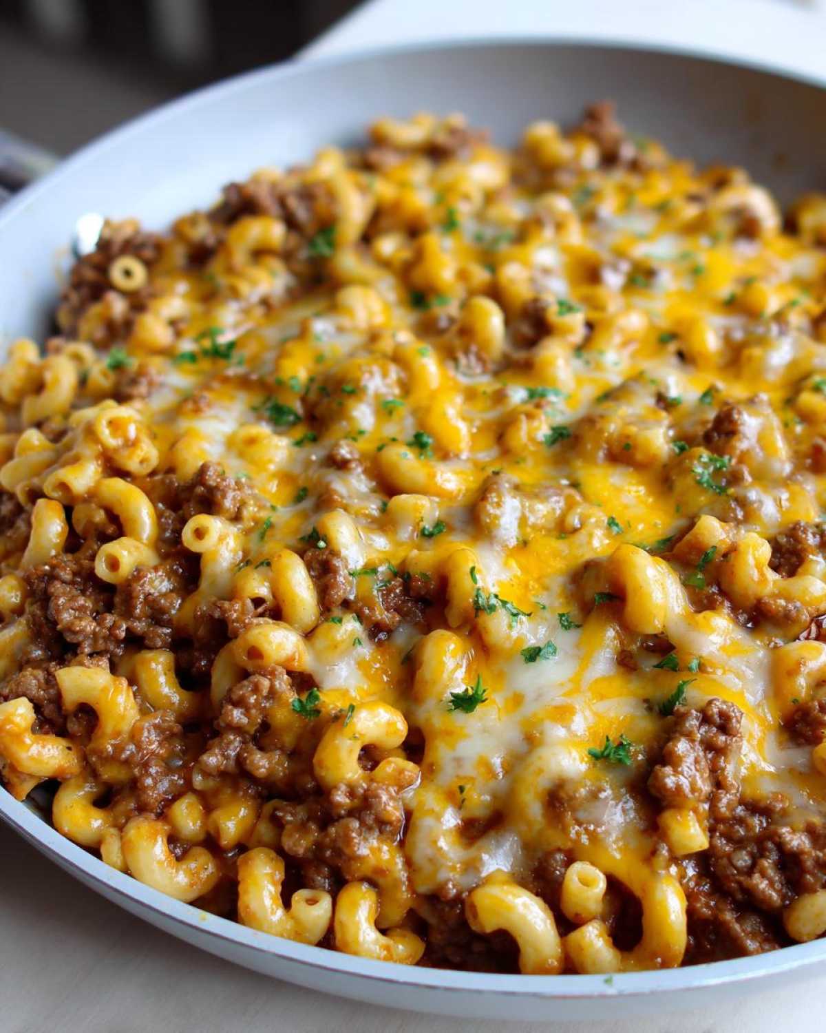 Close-up of a Cheesy Ground Beef Pasta Skillet topped with melted cheddar and mozzarella cheese and parsley.