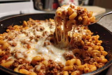 A fork lifts a portion of Cheesy Ground Beef Pasta Skillet with Mozzarella, showing dramatic cheese pulls over the skillet.