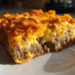 A close-up of a square serving of Cheesy Ground Beef Queso Bake Comfort Dish with a crunchy topping.