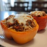 Two vibrant bell peppers, one orange and one red, filled with ground beef, rice, and topped with melted cheese for Cheesy Ground Beef Stuffed Peppers with Rice.