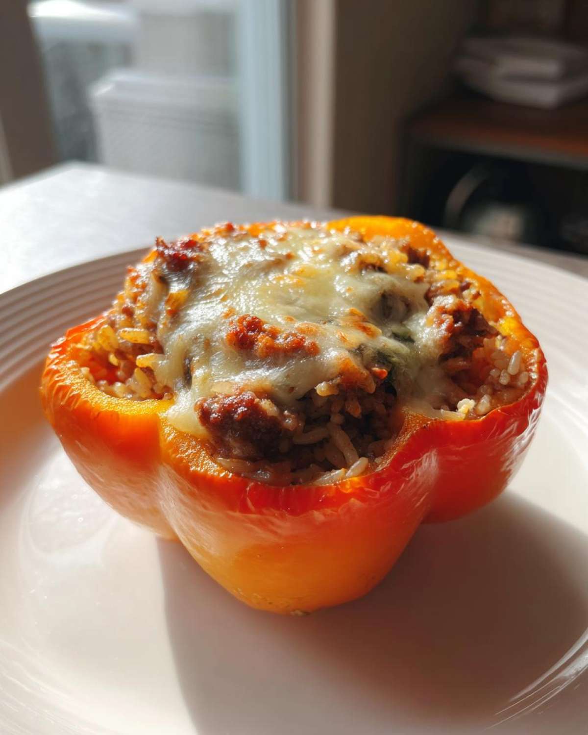 A single, bright orange Cheesy Ground Beef Stuffed Pepper with Rice, topped with melted cheese, sitting on a white plate.