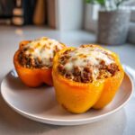 Two halves of bright yellow Cheesy Ground Beef Stuffed Peppers with Rice topped with melted mozzarella cheese on a white plate.