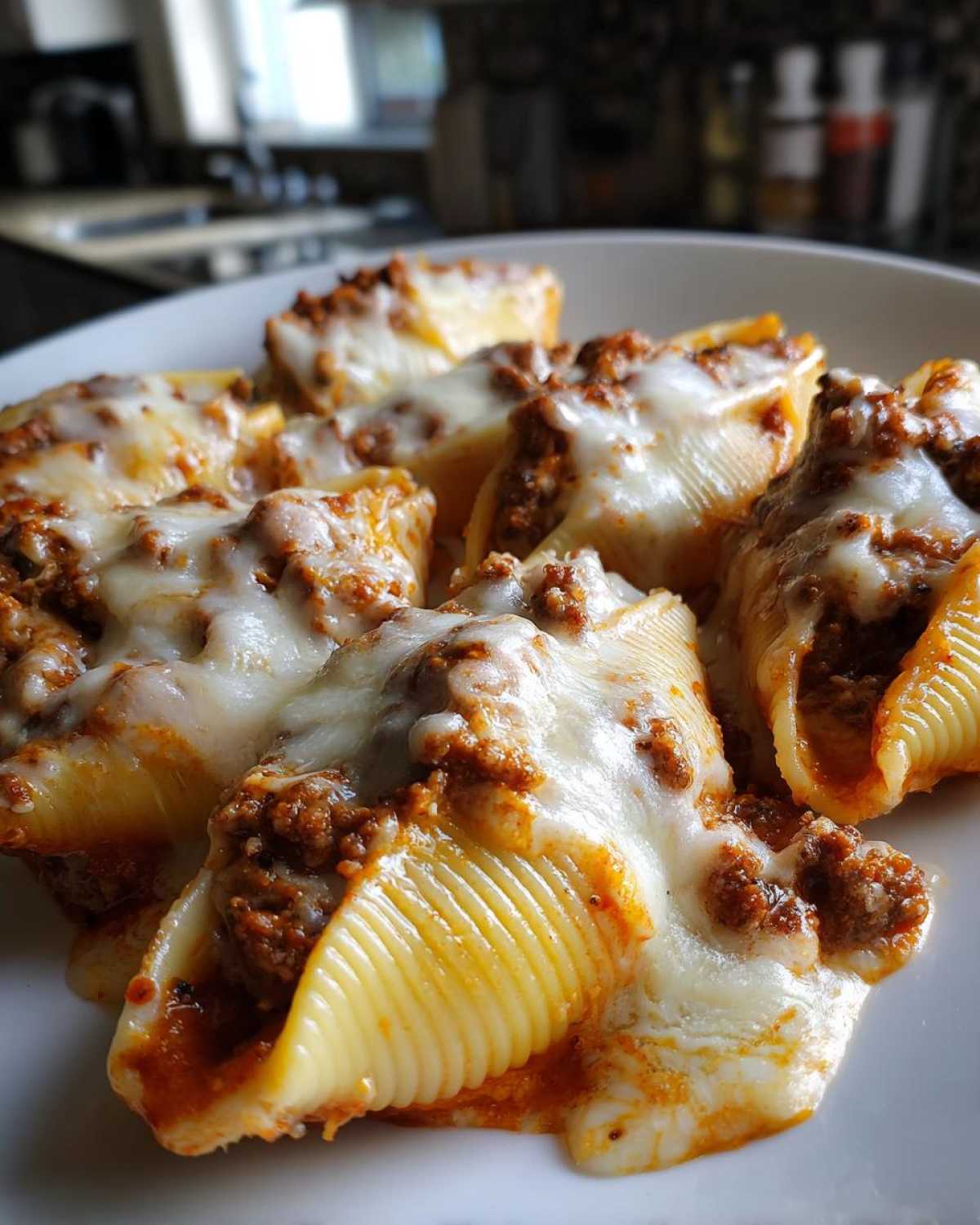 Close-up of Cheesy Ground Beef Stuffed Shells covered in melted mozzarella cheese on a white plate.
