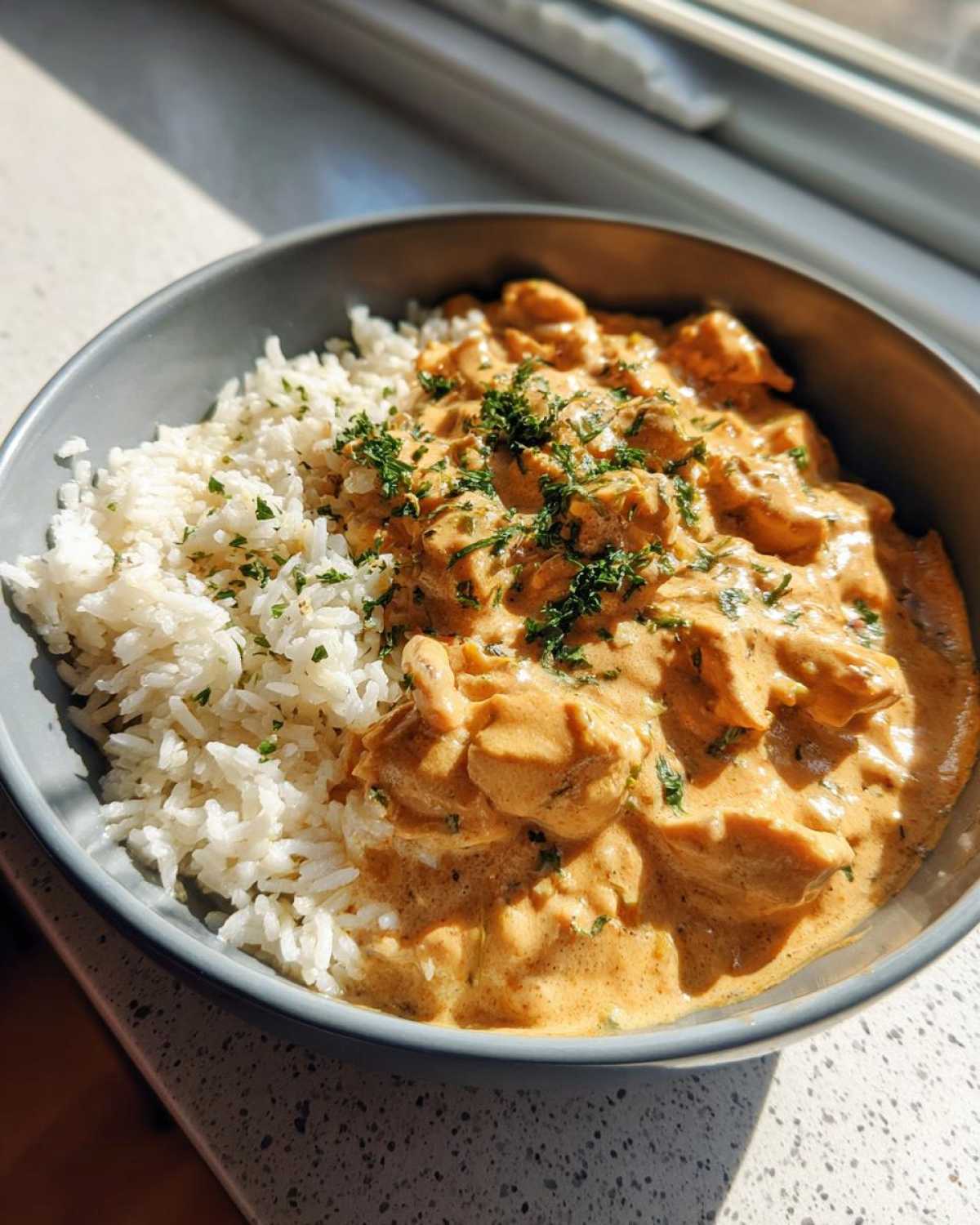 A close-up of Creamy Cajun Chicken Skillet with Rice, served in a gray bowl and garnished with parsley.