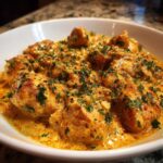 Close-up of tender chicken pieces smothered in a rich, orange-hued Creamy Cajun Chicken Skillet sauce and topped with fresh parsley.