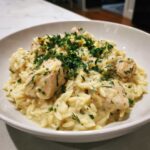 A close-up of creamy lemon chicken orzo topped generously with fresh chopped parsley and dill.