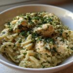 A close-up of a bowl of Creamy Lemon Chicken Orzo generously topped with fresh chopped herbs.