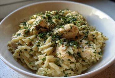 A close-up of a bowl of Creamy Lemon Chicken Orzo generously topped with fresh chopped herbs.