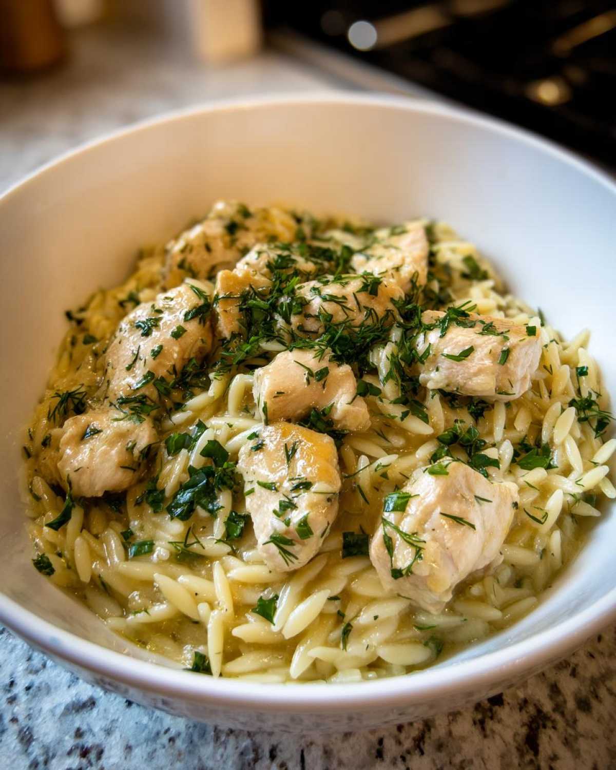 Close-up of Creamy Lemon Chicken Orzo topped with fresh chopped herbs in a white bowl.