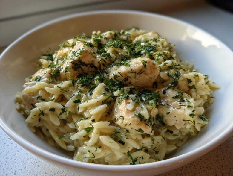 A close-up of a bowl of Creamy Lemon Chicken Orzo generously topped with fresh chopped herbs.