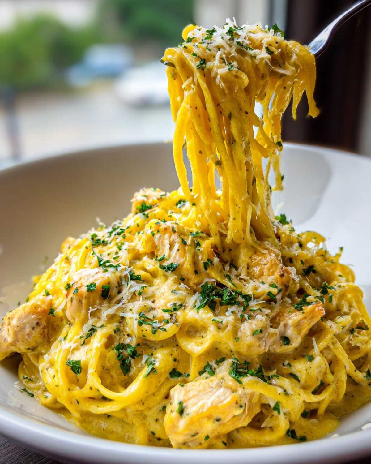 A fork lifting a tangle of spaghetti coated in a rich, yellow sauce from a bowl of Creamy Lemon Chicken Pasta with Parmesan.