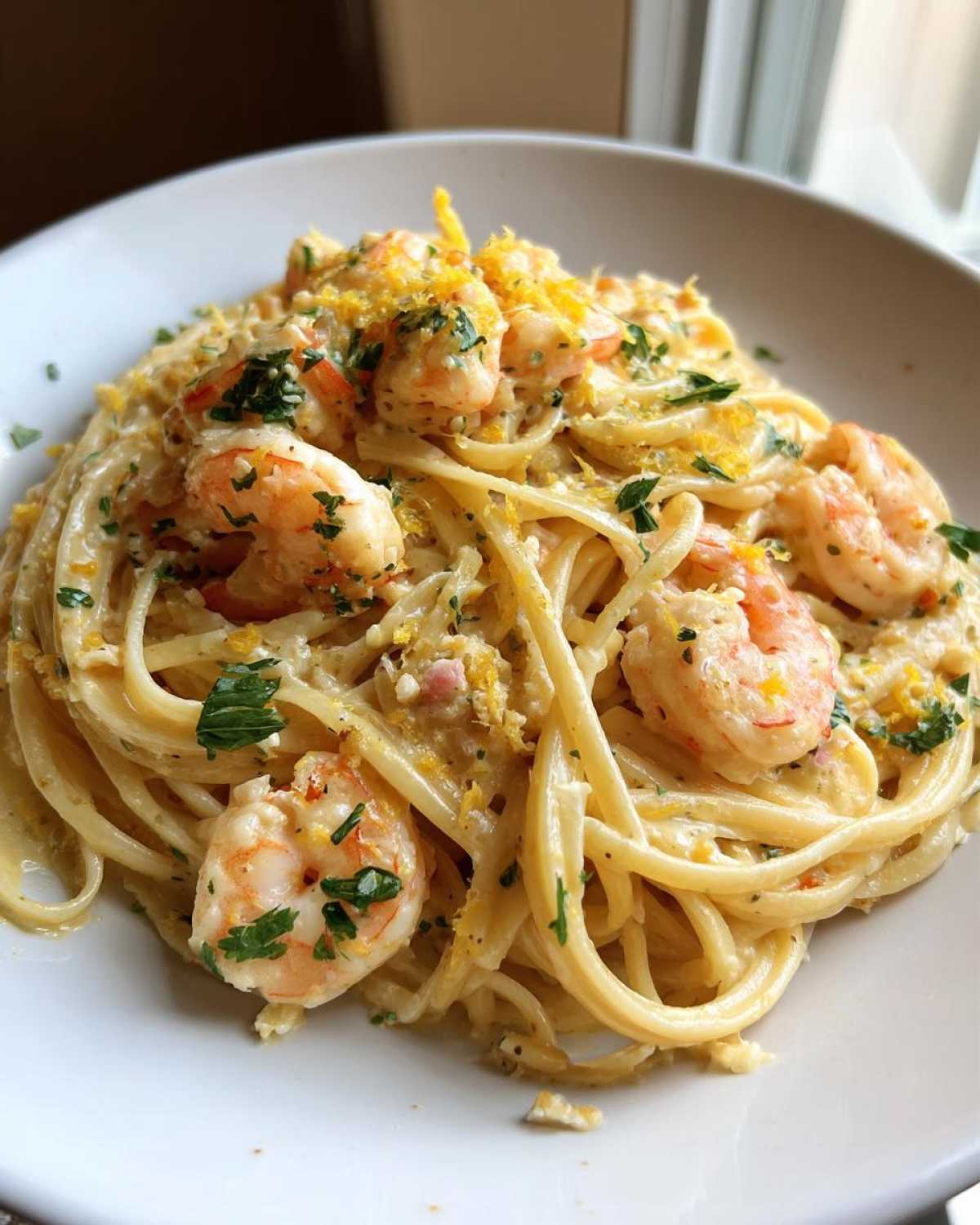 Close-up of a white bowl filled with Creamy Lemon Garlic Shrimp Pasta, topped with lemon zest and parsley.