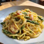 A close-up of Creamy Lemon Shrimp Pasta Fresh Flavor mixed with bright green asparagus spears.