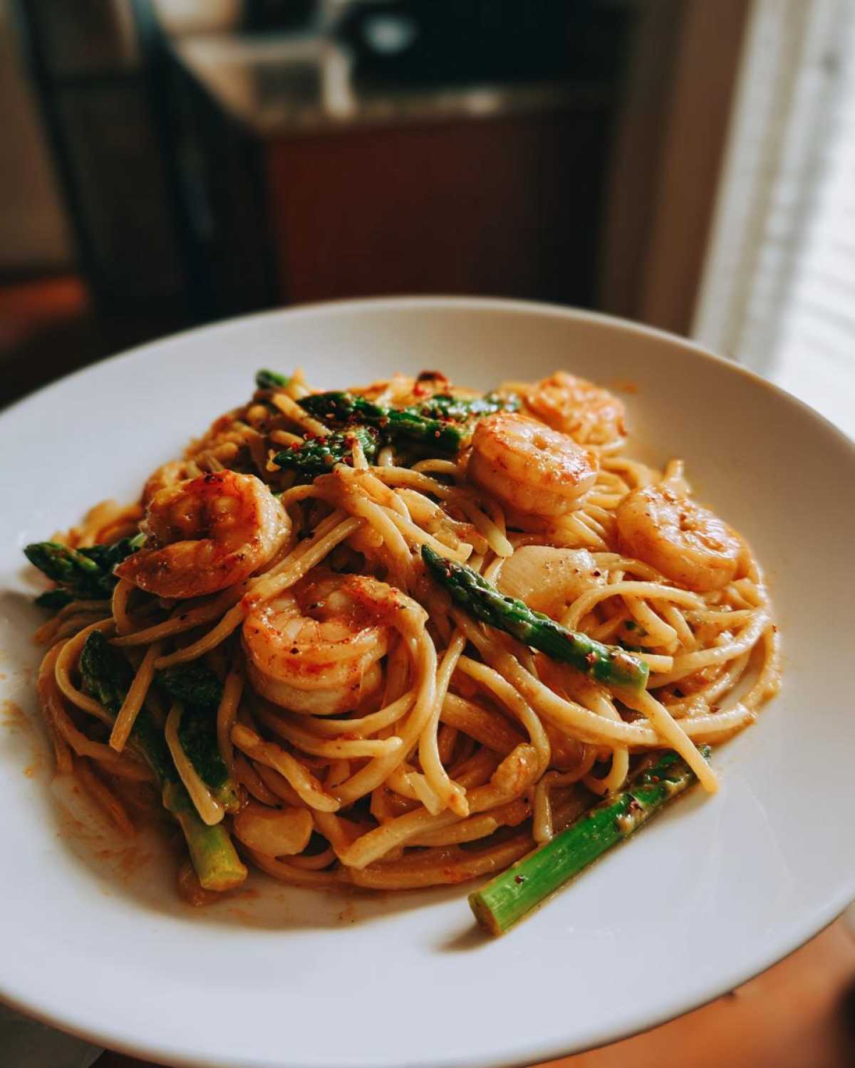 A close-up of a white plate holding Creamy Lemon Shrimp Pasta Fresh Flavor mixed with bright green asparagus spears and plump shrimp.