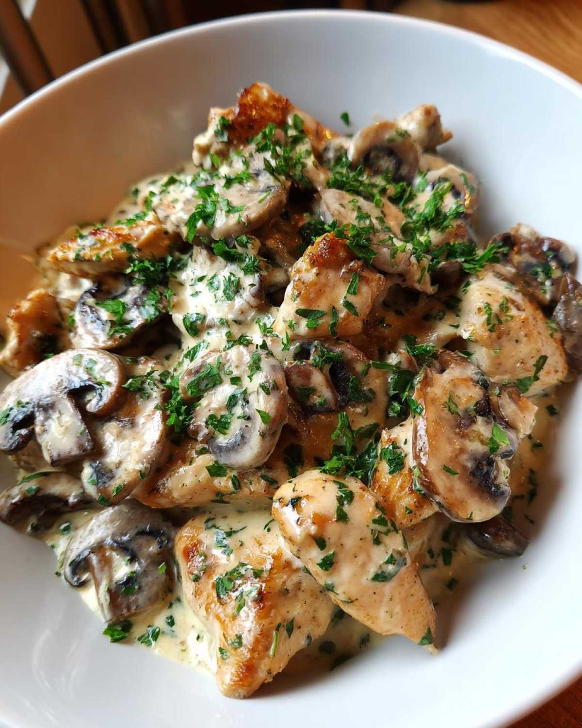 Close-up of pan-seared chicken pieces and sliced mushrooms coated in a rich sauce, garnished with parsley, part of the Creamy Mushroom Alfredo Chicken Skillet.