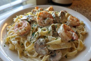 A close-up of Creamy Mushroom Alfredo Shrimp Skillet served over fettuccine pasta, garnished with parsley.