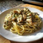 A close-up of a white plate piled high with Creamy Mushroom Chicken Alfredo Pasta, garnished with parsley.