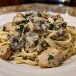 A close-up of a white plate piled high with Creamy Mushroom Chicken Alfredo Pasta, topped with mushrooms and parsley.