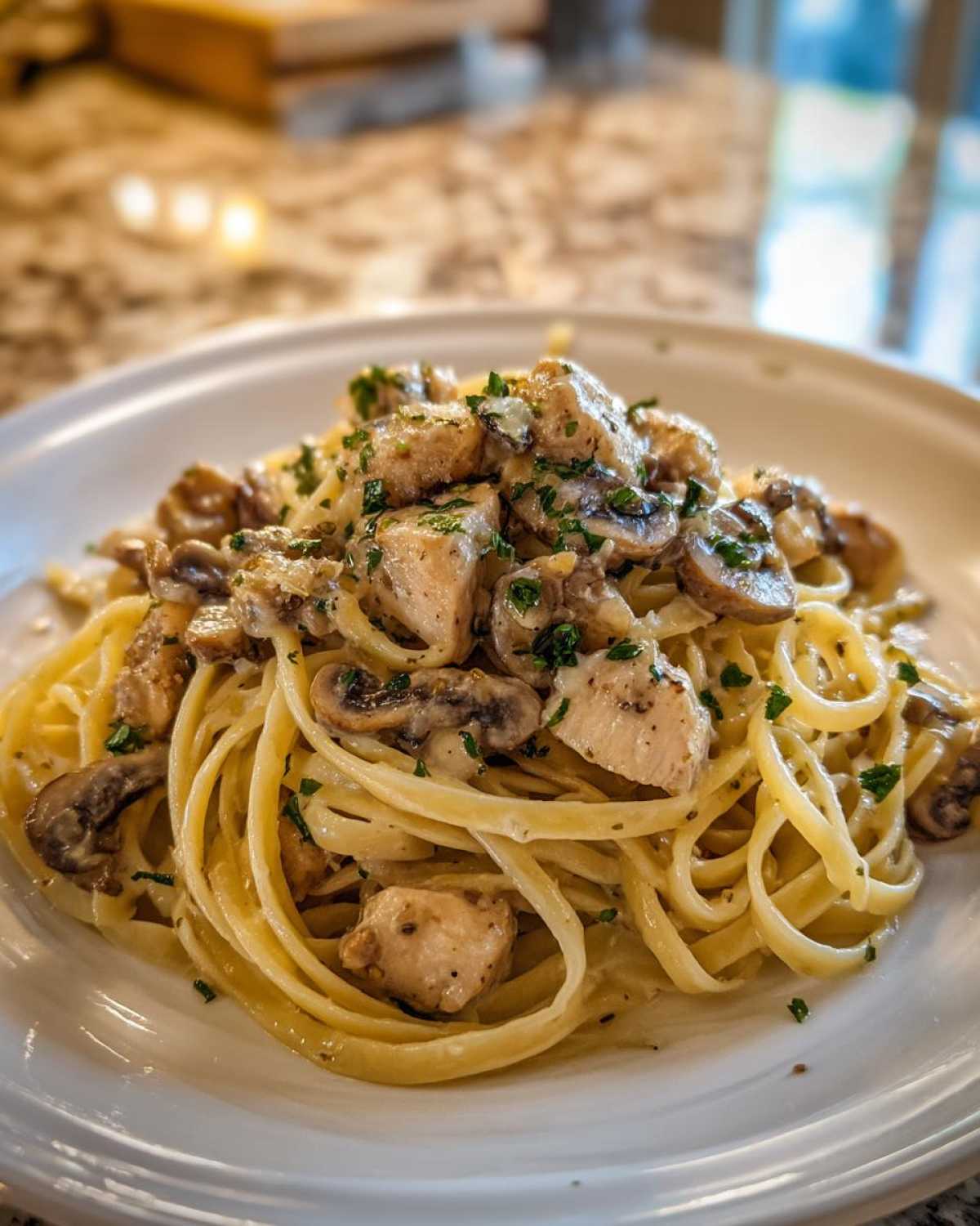 A close-up of a serving of Creamy Mushroom Chicken Alfredo Pasta with fettuccine noodles, chicken chunks, and sliced mushrooms.