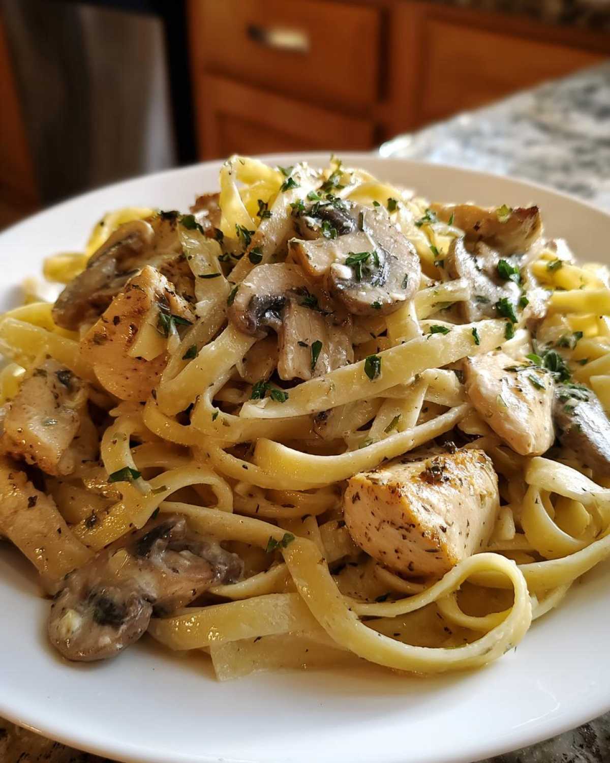 Close-up of a white plate filled with Creamy Mushroom Chicken Alfredo Pasta, featuring fettuccine, seasoned chicken chunks, and sliced mushrooms.