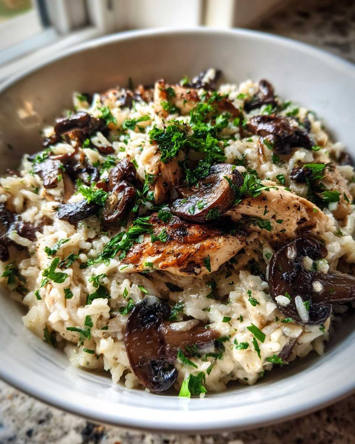 A close-up bowl of Creamy Mushroom Chicken and Rice Skillet topped with sautéed mushrooms and fresh parsley.
