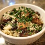 A close-up of a white bowl filled with Creamy Mushroom Chicken and Rice Skillet, topped with fresh parsley.