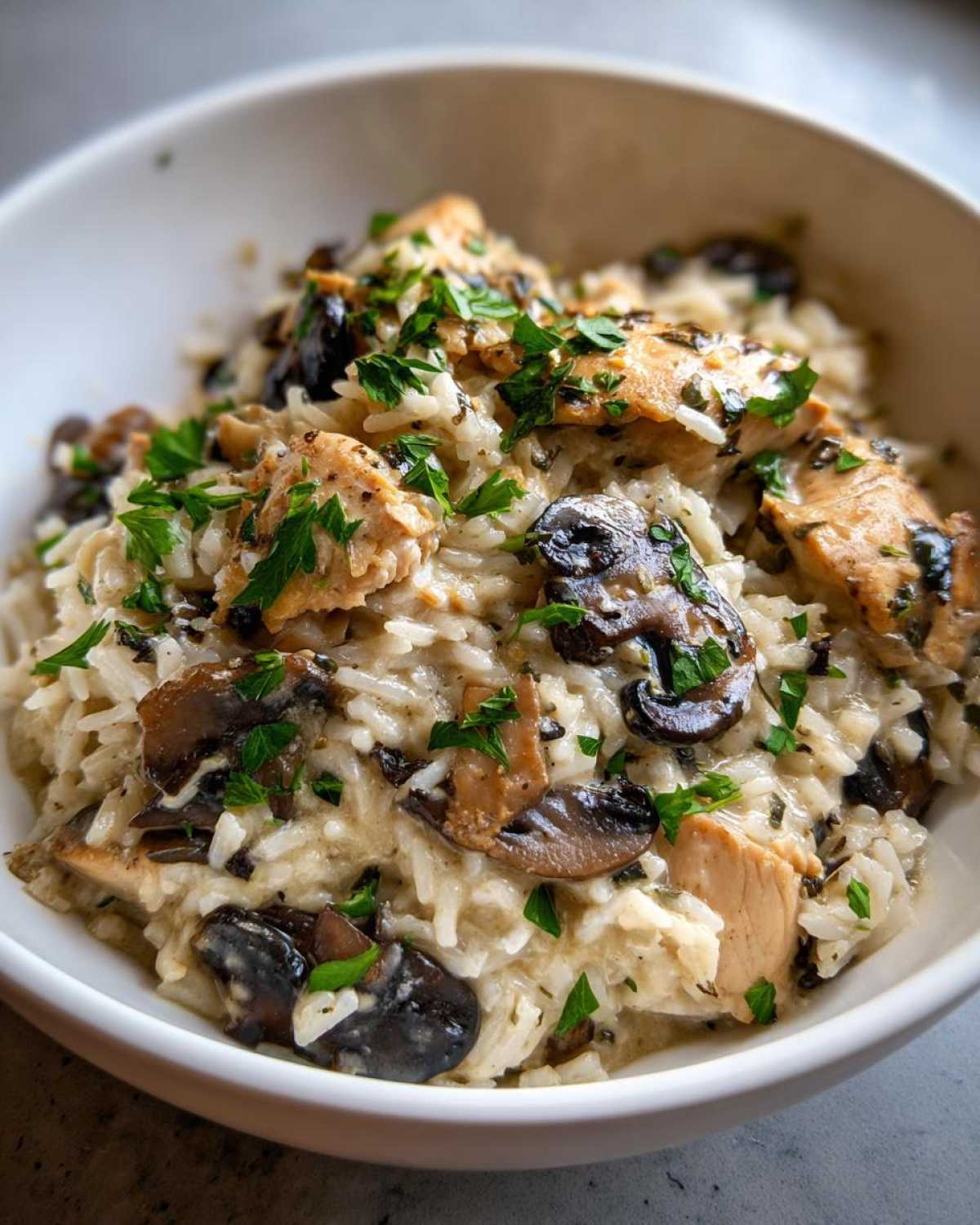 Close-up of a white bowl filled with Creamy Mushroom Chicken and Rice Skillet, garnished with fresh parsley.