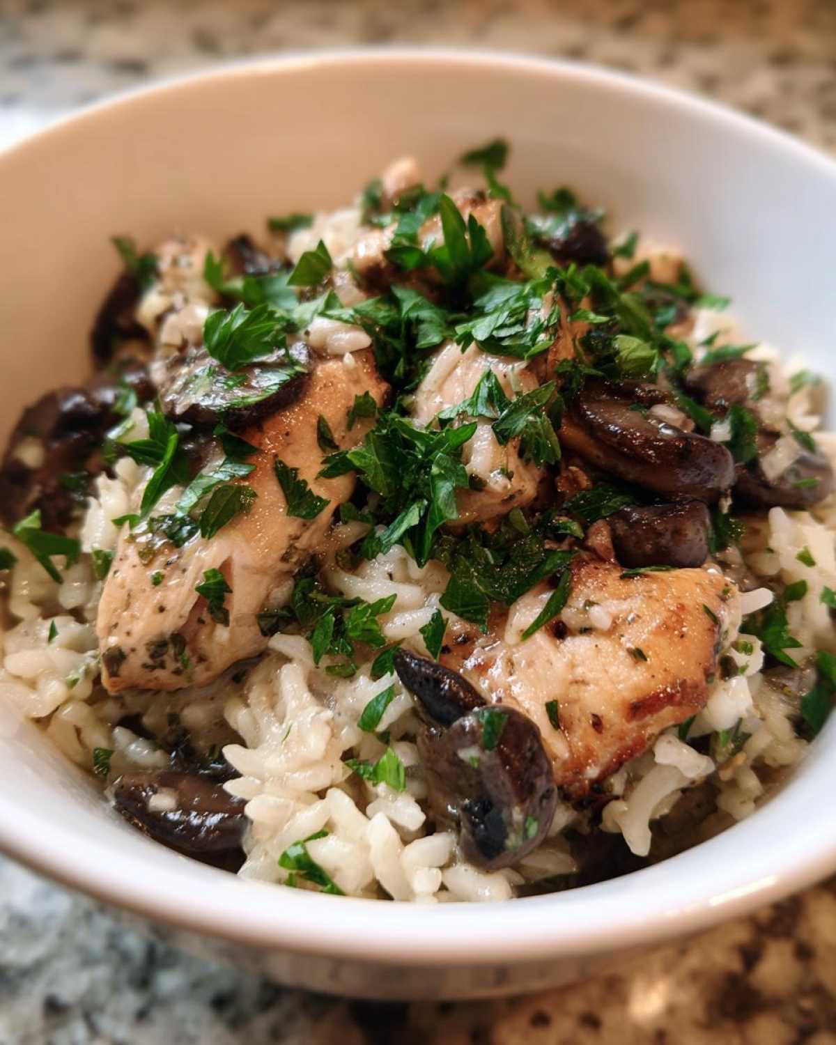 Close-up of a white bowl filled with Creamy Mushroom Chicken and Rice Skillet, topped with fresh parsley.