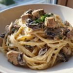 A close-up of a bowl filled with Creamy Mushroom Chicken Pasta with Garlic Sauce, featuring fettuccine, chunks of chicken, and sliced mushrooms.