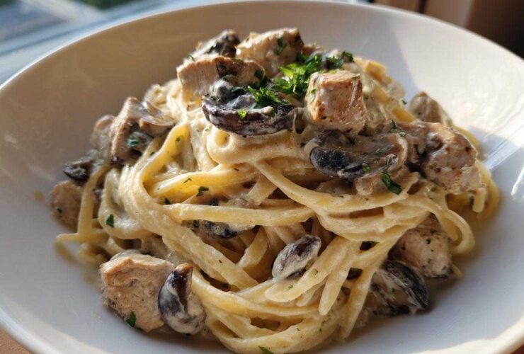 A close-up of a bowl filled with Creamy Mushroom Chicken Pasta with Garlic Sauce, featuring fettuccine, chunks of chicken, and sliced mushrooms.