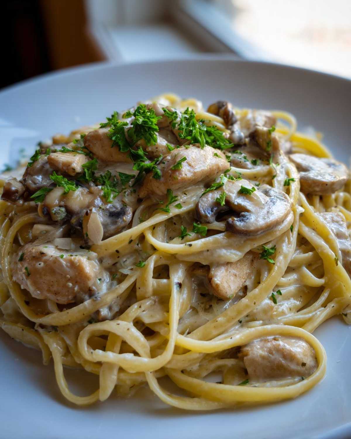Close-up of Creamy Mushroom Chicken Pasta with Parmesan, featuring fettuccine, chicken pieces, sliced mushrooms, and parsley garnish.