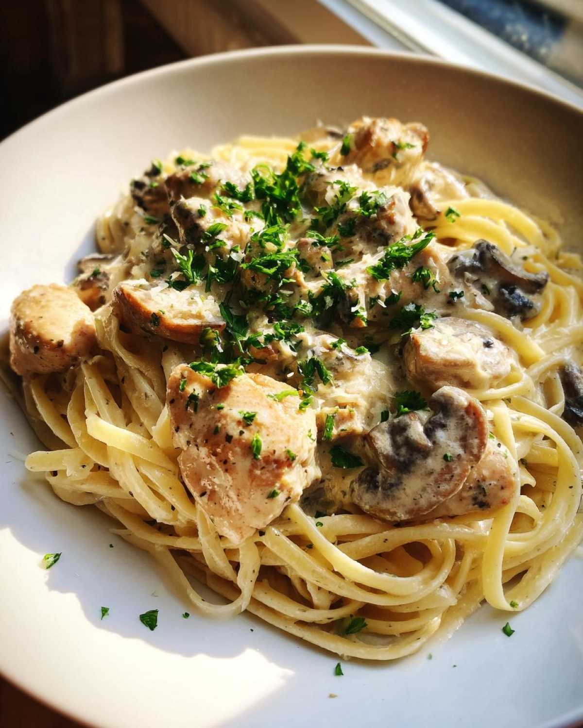 A close-up of a bowl of Creamy Mushroom Chicken Pasta with Parmesan, topped with fresh parsley.