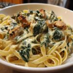Close-up of a bowl filled with Creamy Spinach Alfredo Pasta with Chicken tossed in a rich white sauce.