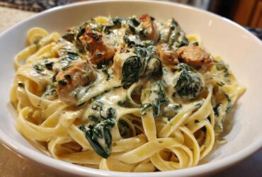 Close-up of a bowl filled with Creamy Spinach Alfredo Pasta with Chicken tossed in a rich white sauce.
