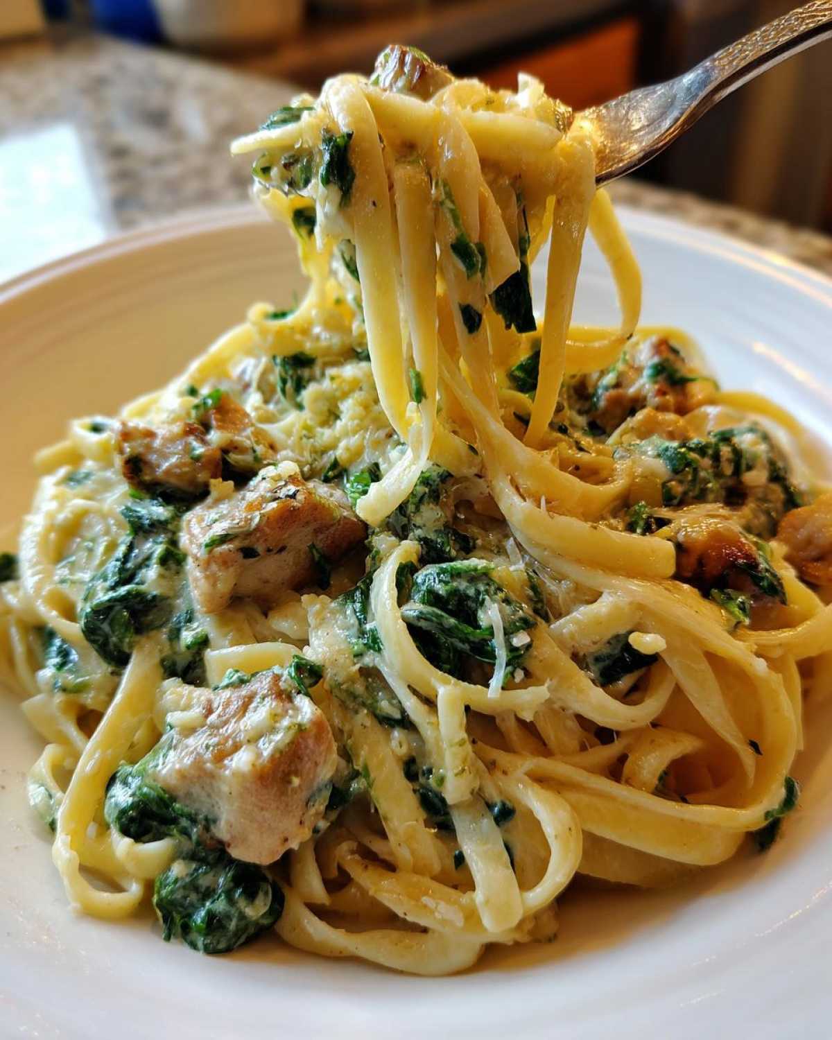 A fork lifting fettuccine noodles coated in creamy sauce, spinach, and chicken from a plate of Creamy Spinach Alfredo Pasta with Chicken.