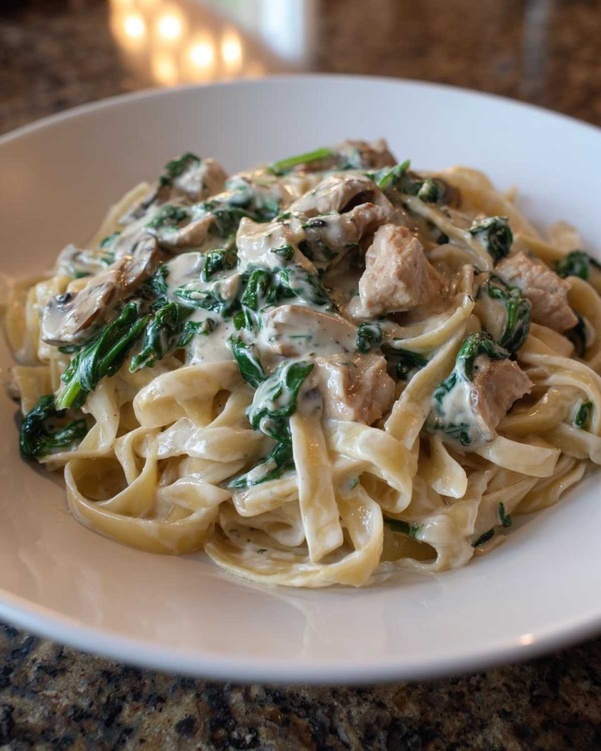 Close-up of Creamy Spinach Alfredo Pasta with Chicken and mushrooms served in a white bowl.